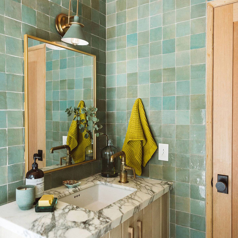 Bathroom with green tiled walls, marble countertop, and gold-framed mirror.