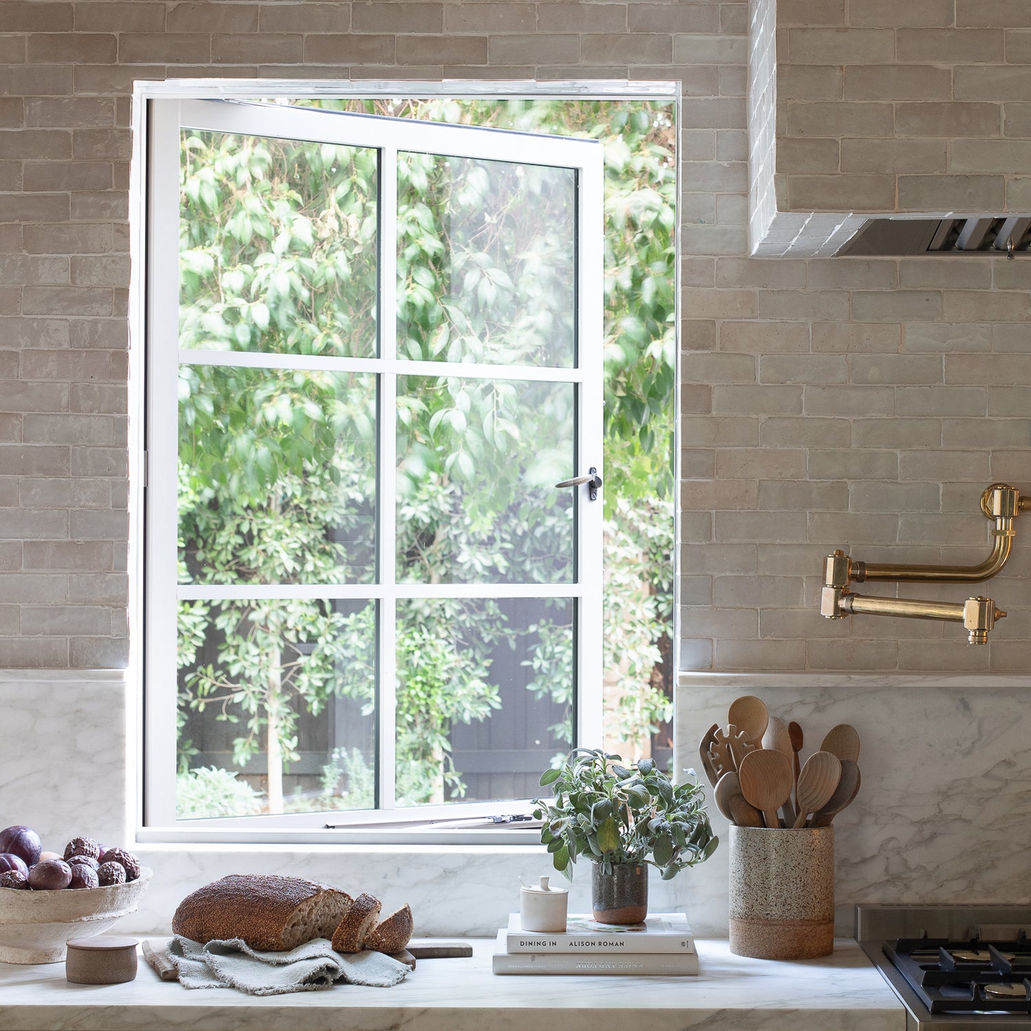 Modern kitchen with a window view of greenery, wooden utensils, and a loaf of bread on the counter.
