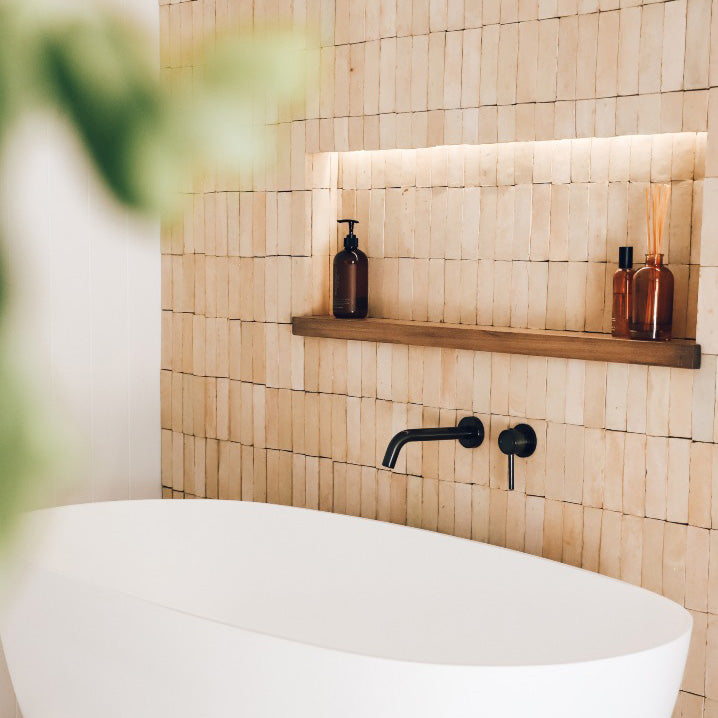 Bathroom with wooden tiles, a white bathtub, and a wooden shelf with bottles.