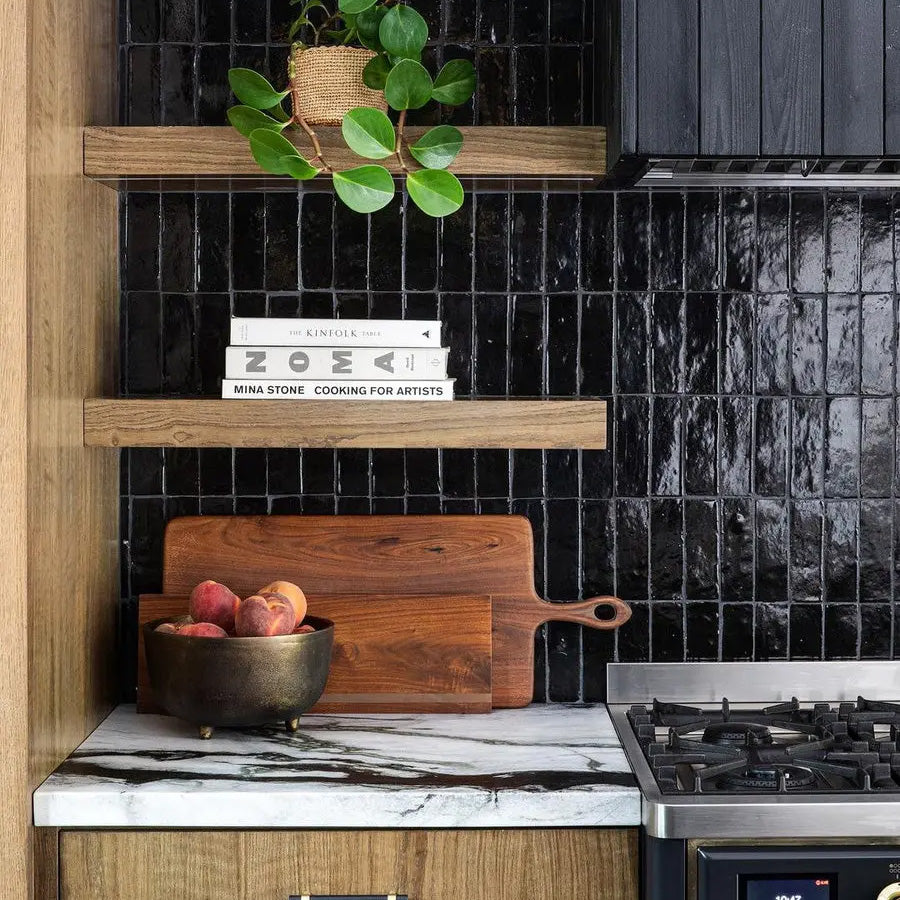 Modern kitchen with black tiled wall, marble countertop, and wooden cutting board.