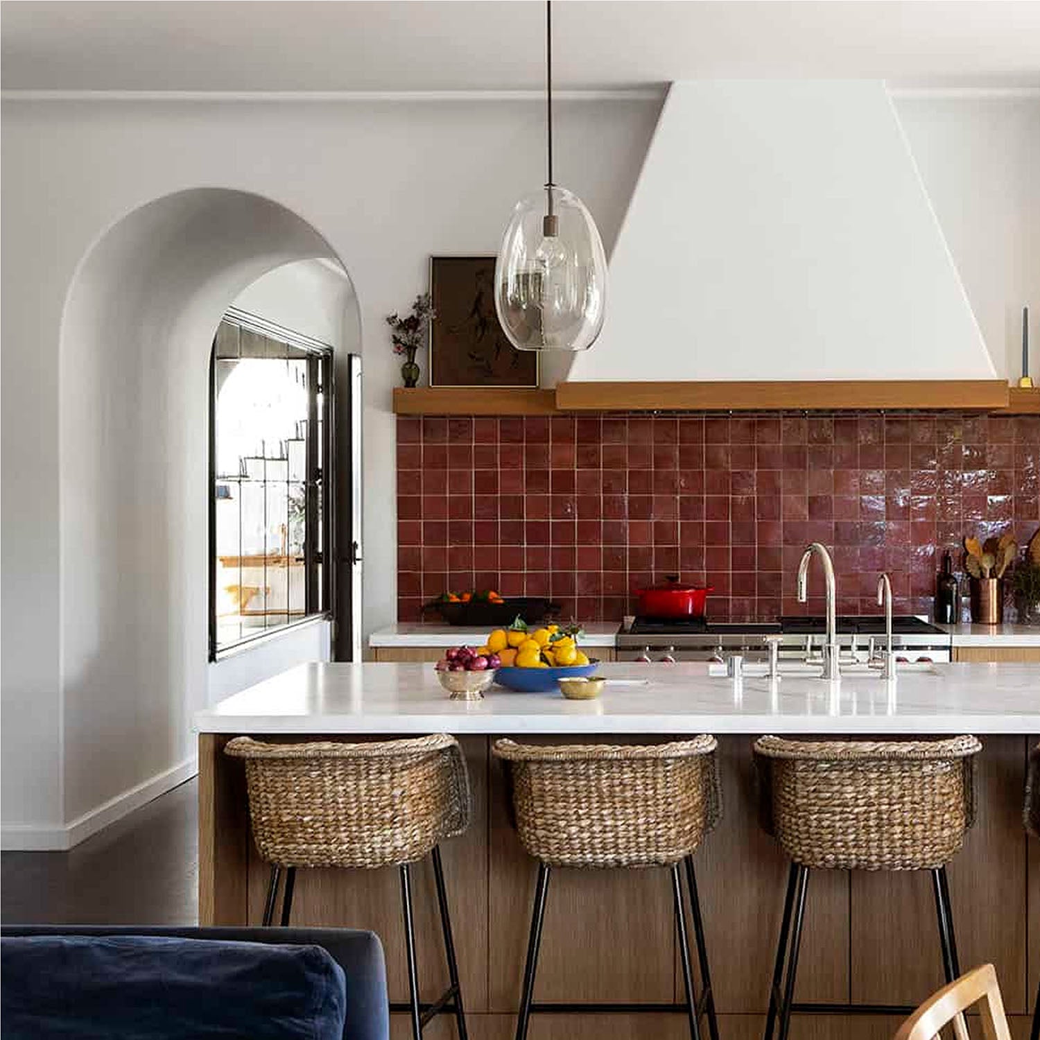 Modern kitchen with red tiled backsplash, white countertops, and wicker bar stools.