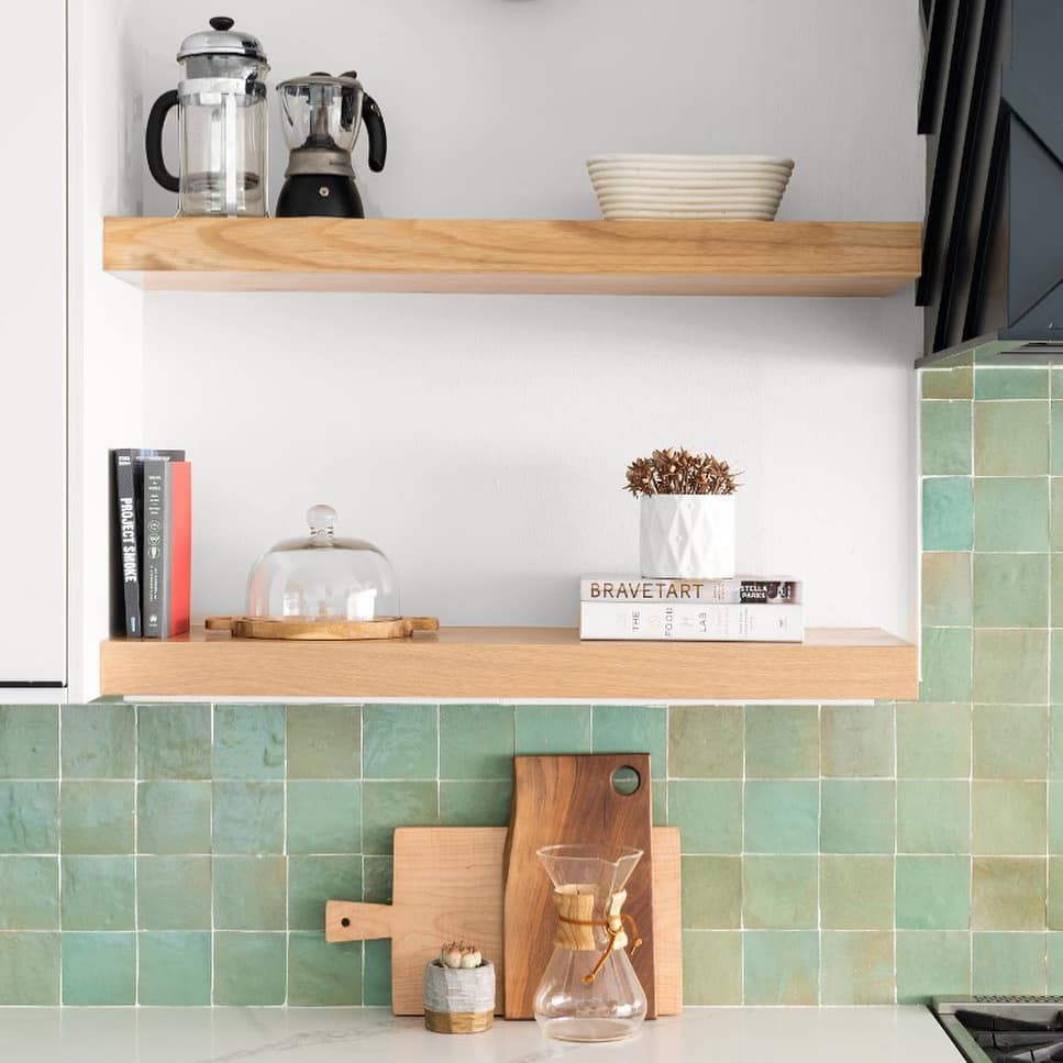 Kitchen shelves with books, a coffee maker, and a plant against a tiled wall.