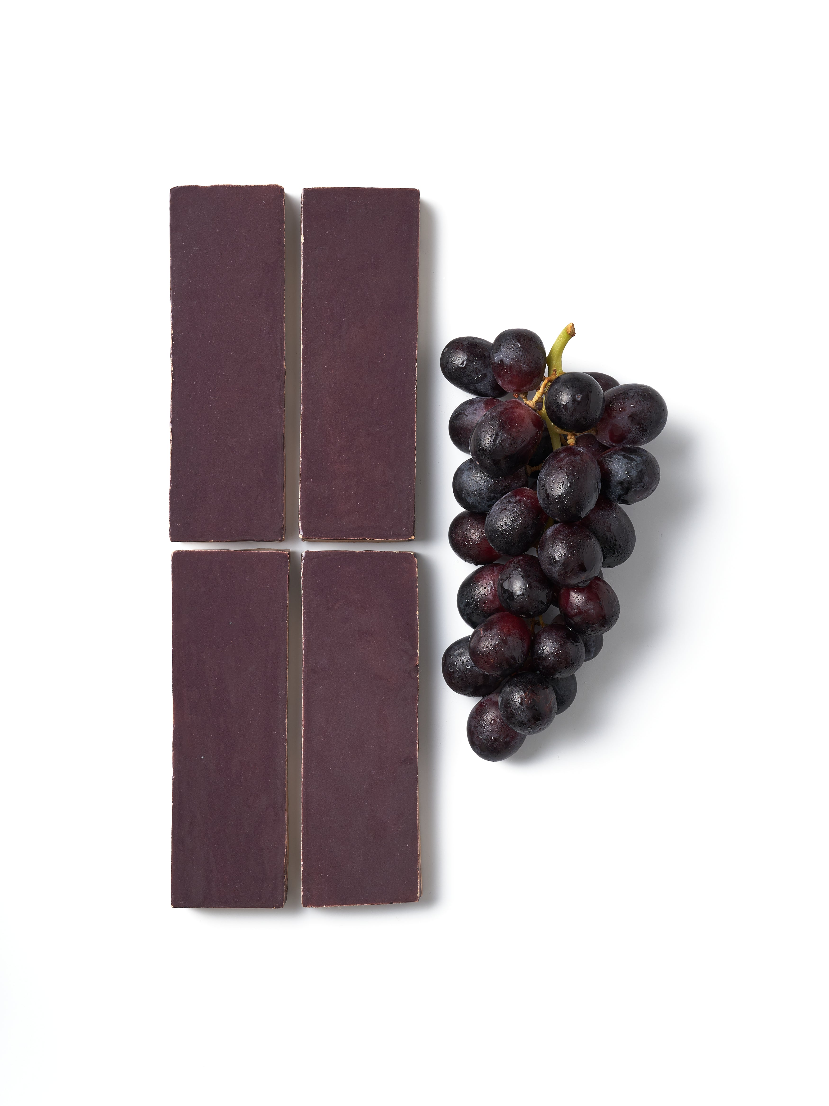 Four dark chocolate bars with a bunch of grapes on a white background